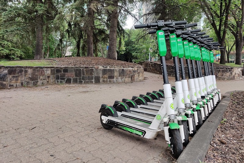 Electric scooters all the same colour and make, lined up in a rack along a path.