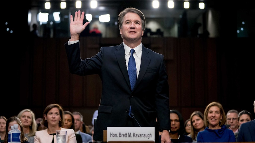 Brett Kavanaugh stands with one hand in the air as he is sworn in.
