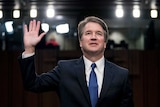 Brett Kavanaugh stands with one hand in the air as he is sworn in.