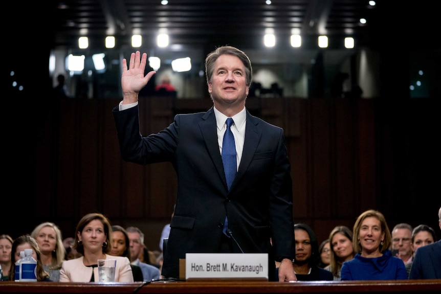 Brett Kavanaugh stands with one hand in the air as he is sworn in.