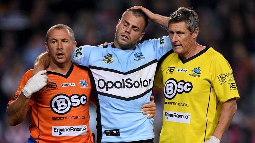 A Sharks player is helped from the field by two men.