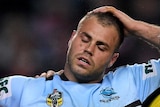 A Sharks player is helped from the field by two men.