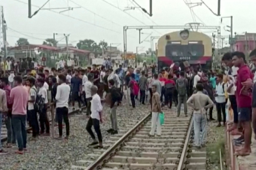 Crowds of men block train tracks.