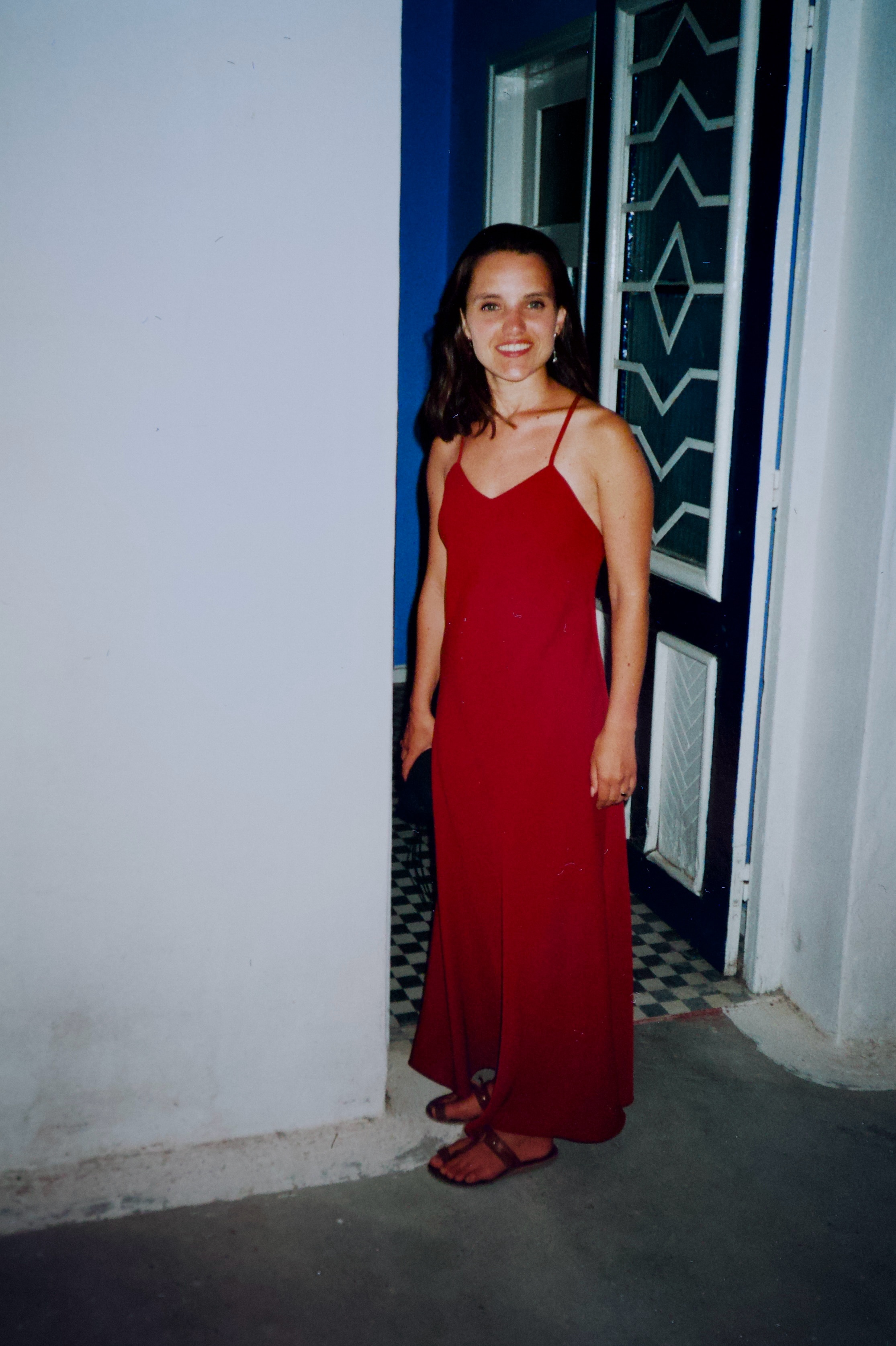 Una mujer joven se encuentra frente a una puerta con un vestido largo rojo.