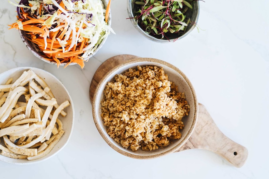 Four bowls of ingredients including tofu strips, shredded vegetables, microgreens and fried brown rice, for a crunchy salad.