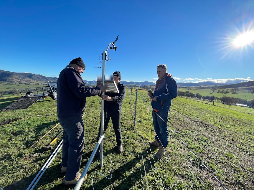 Three people work to mount a solar panel on a metal frame.