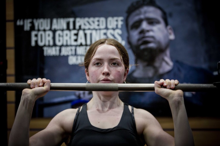 A young woman holds up a heavy powerlifting bar at the gym.