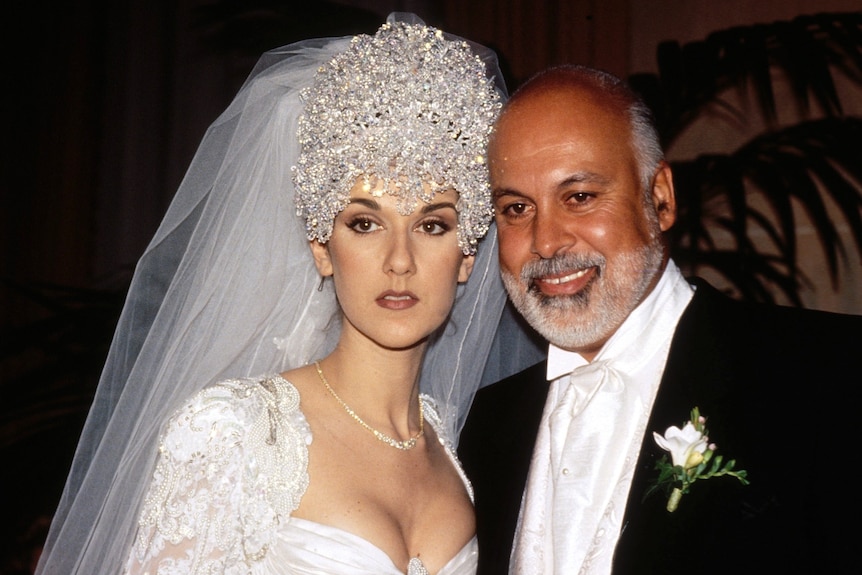 Celine Dion in an enormous sparkling white headress and veil, next to her husband in a tuxedo