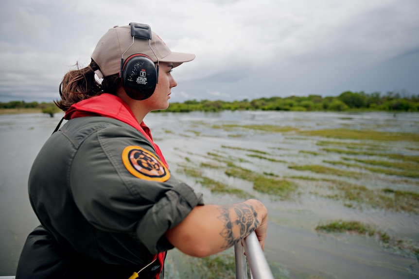 A woman leans on a boat railing and looks out over floodplains