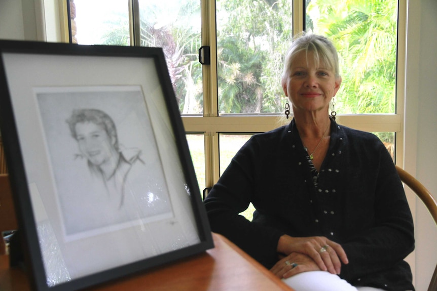 A woman sits beside a drawing of her 21-year-old son
