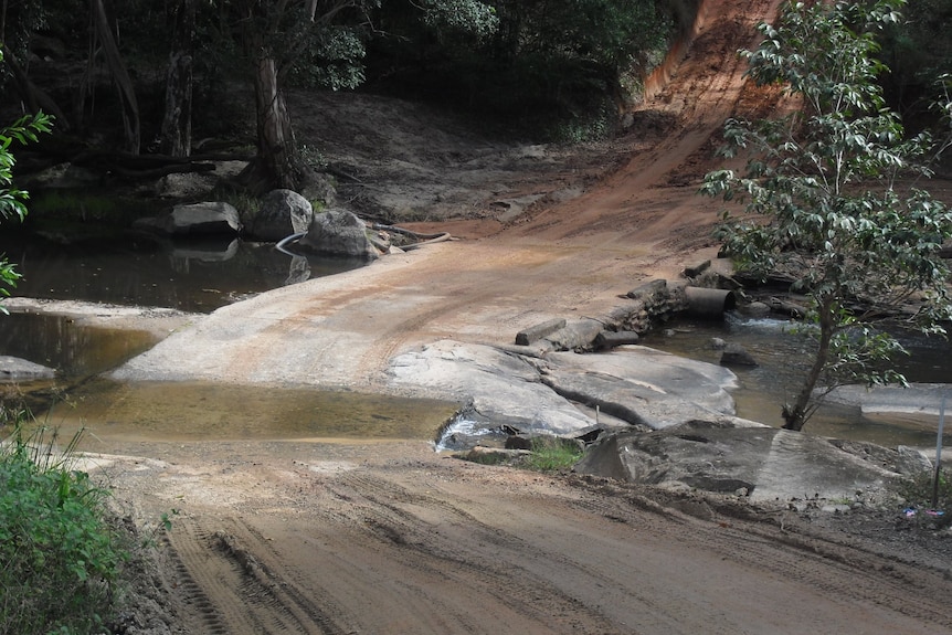 An unsealed road with a creek crossing ahead of a steep incline.