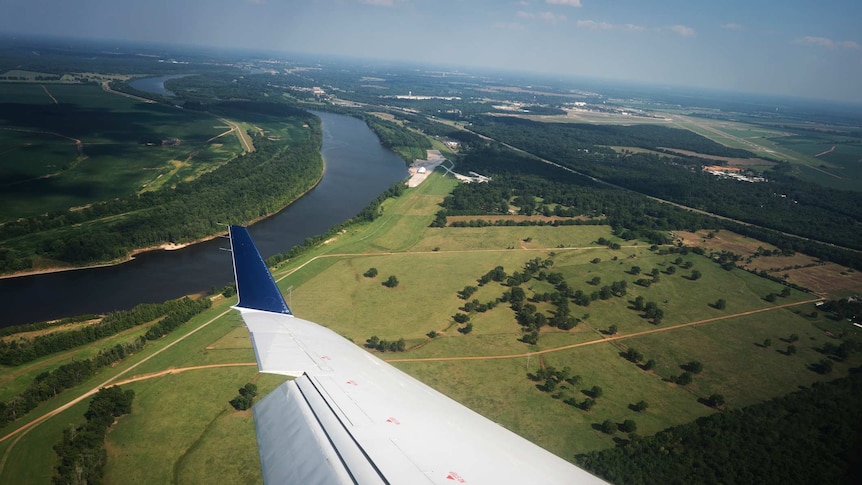 View from inside a plane window looking over the wing to green farmland below.