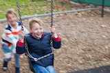 A girl pushes a boy on a swing.