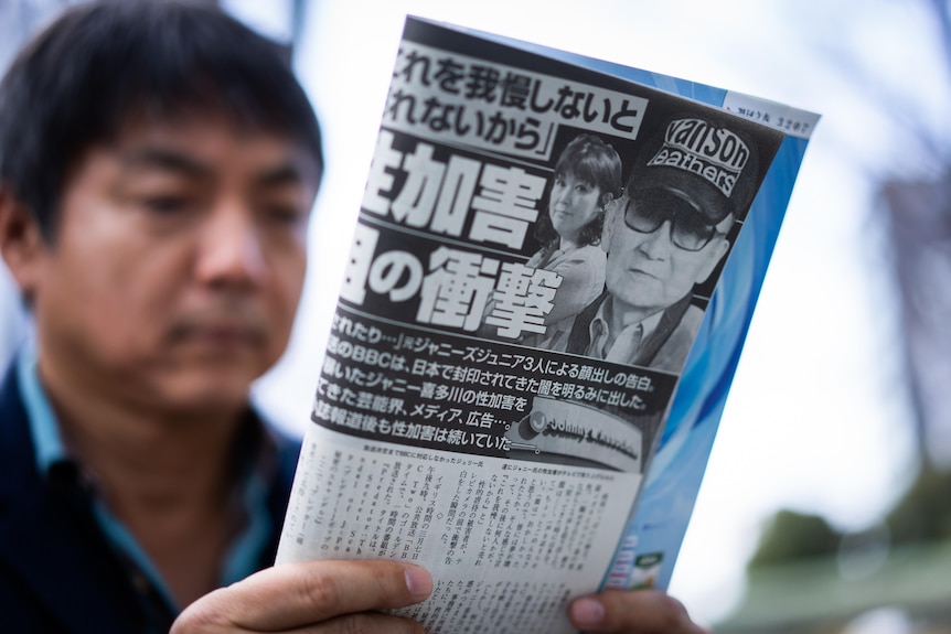 A man reads a folded up magazine with a black-and-white image of Johnny Kitagawa