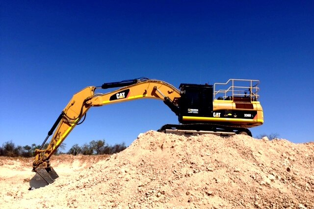 A close shot of a large excavator on a mound of rocks. Blue sky in the background.