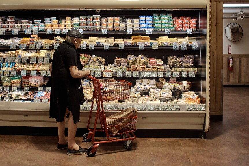 A man wheels a trolley in front of a refrigerated aisle in a supermarket.