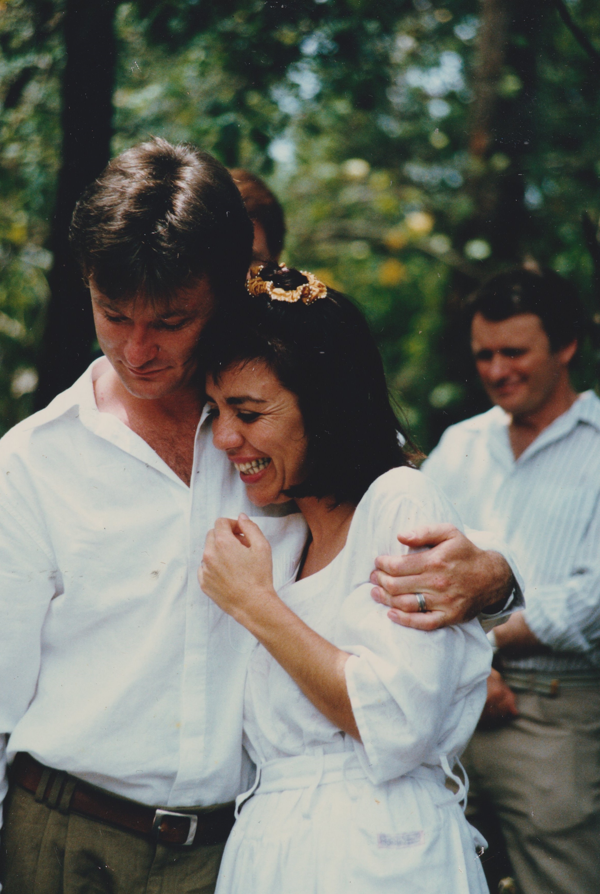 A man and woman dressed in white hold each other smiling.