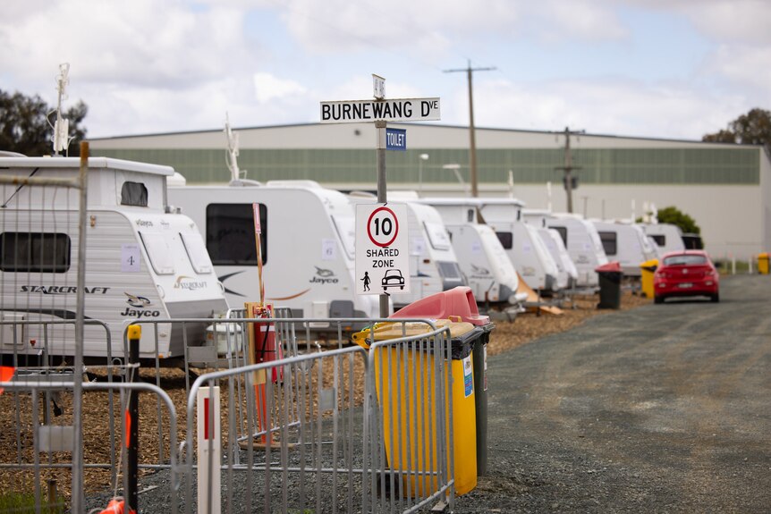 A row of caravans with a street sign saying Burnewang Drive, 10k shared zone, sign of pedestrian and car. Bins outside.