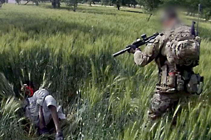 An SAS soldier points gun at Afghan man who is lying on the ground. The soldier's head is blurred out. 