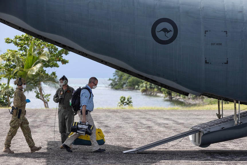 health staff wearing blue shirts or military attire walk up ramp onto a plane