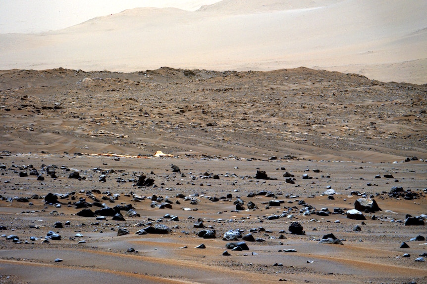 A red-sand plain, strewn with shiny black rocks. in the distance, a large orange sheet of fabric