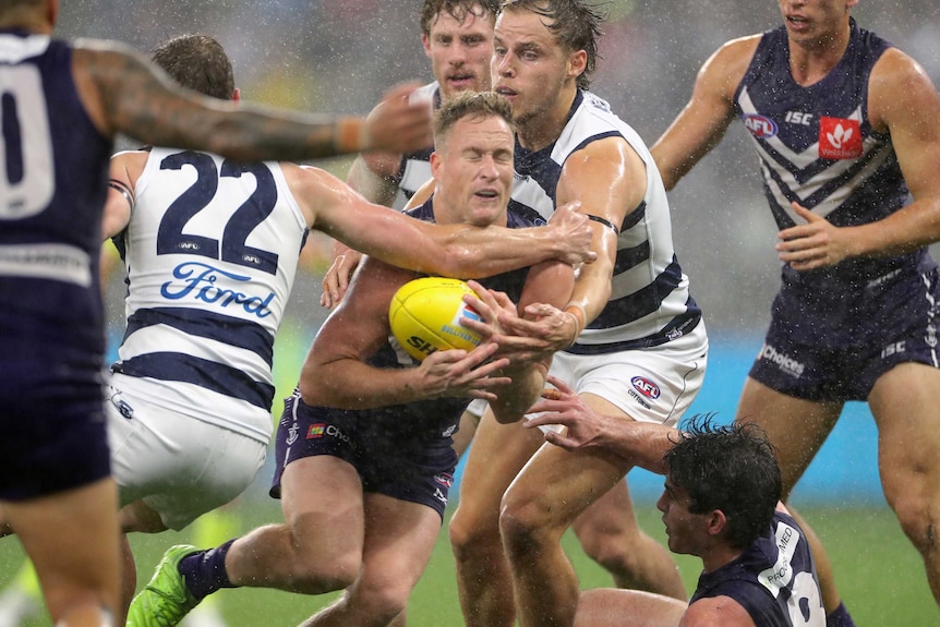 Brandon Matera grimaces as he is tackled by two Geelong players