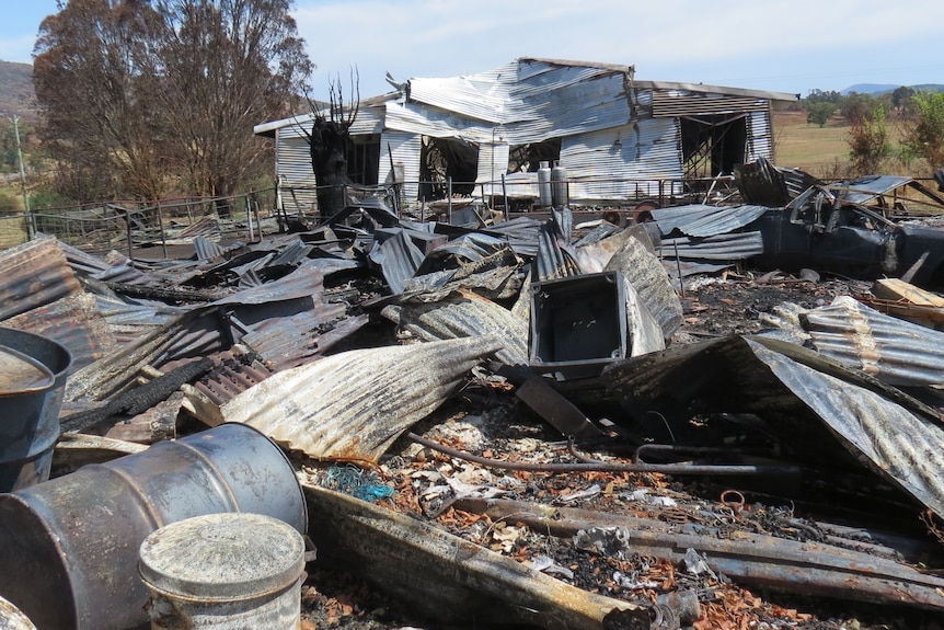 A pile of burnt corrugated iron in front of a dwelling on a hill.