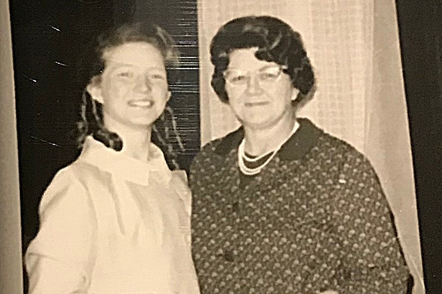 A photo of a girls standing with her mother in the 1960s, wearing smart clothing and holding handbags.