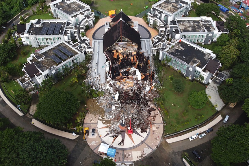 Half of a building has collapsed and lays in a pile of rubble as seen from the air.