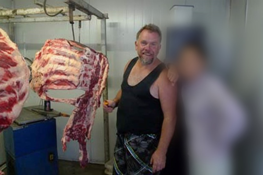 A man and person with a blurred face next to hanging horse carcasses.