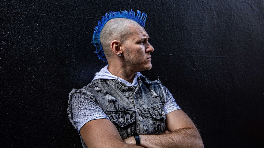 A man in a blue mohawk against a black background