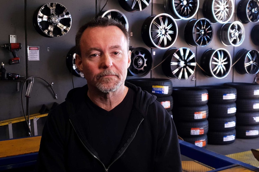 A man stands in front of a wall covered in car wheels.