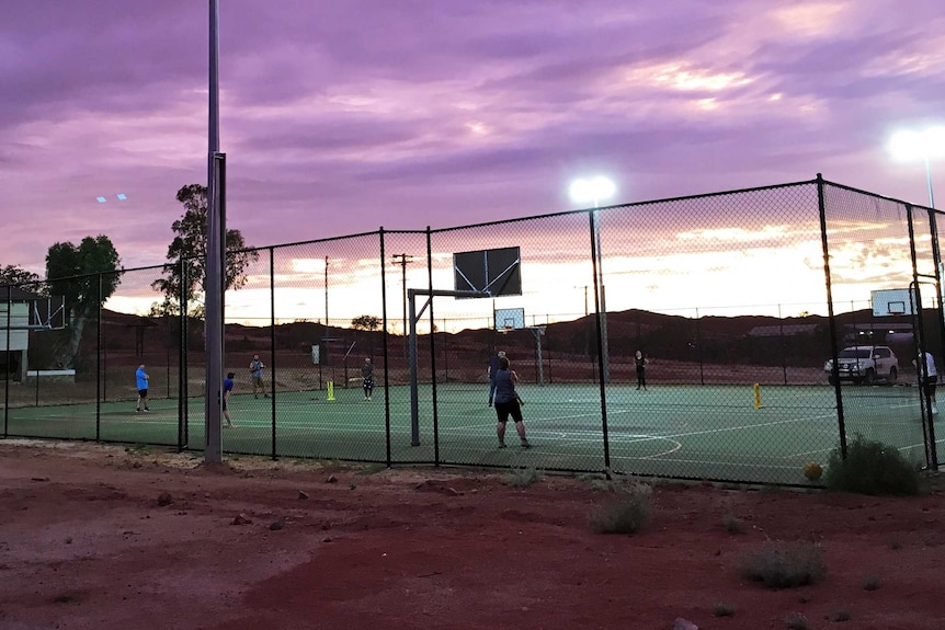 Purple sunset clouds over the lit-up basketball courts where locals play indoor cricket, outdoors.
