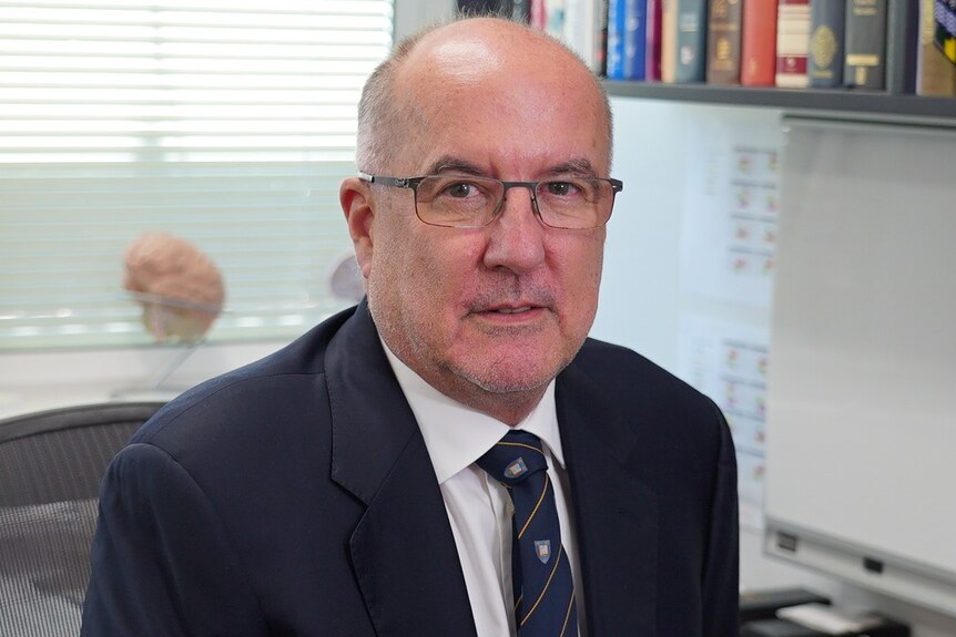 Neurologist Professor Peter Silburn sits at a desk in his practice office in Brisbane.