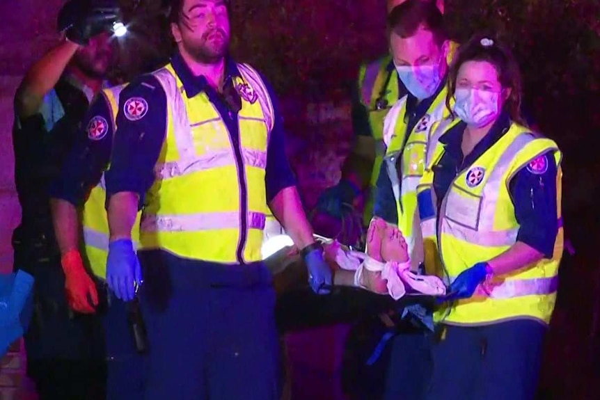 A boy's feet can be seen on the end of a stretcher, being carried by several ambulance officers