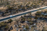 A drone photo above the highway with bush burnt on either side and a car and caravan travelling through.