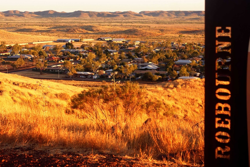 A photo of Roebourne looking down from a hill at sunset, with a sign saying Roebourne in the foreground