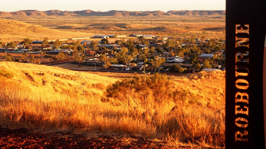 A photo of Roebourne looking down from a hill at sunset, with a sign saying Roebourne in the foreground