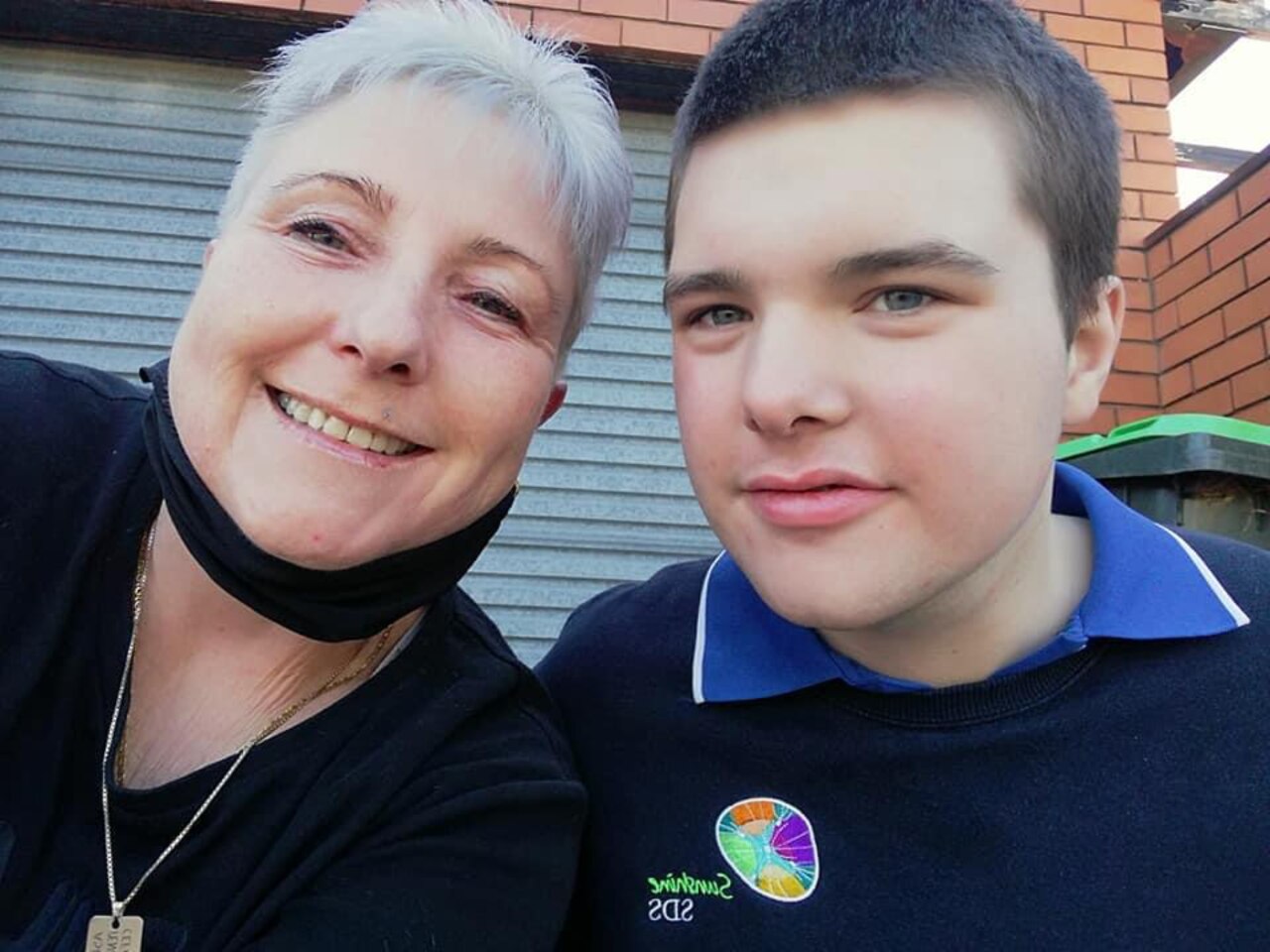 Boy in school uniform with woman smiling by side.