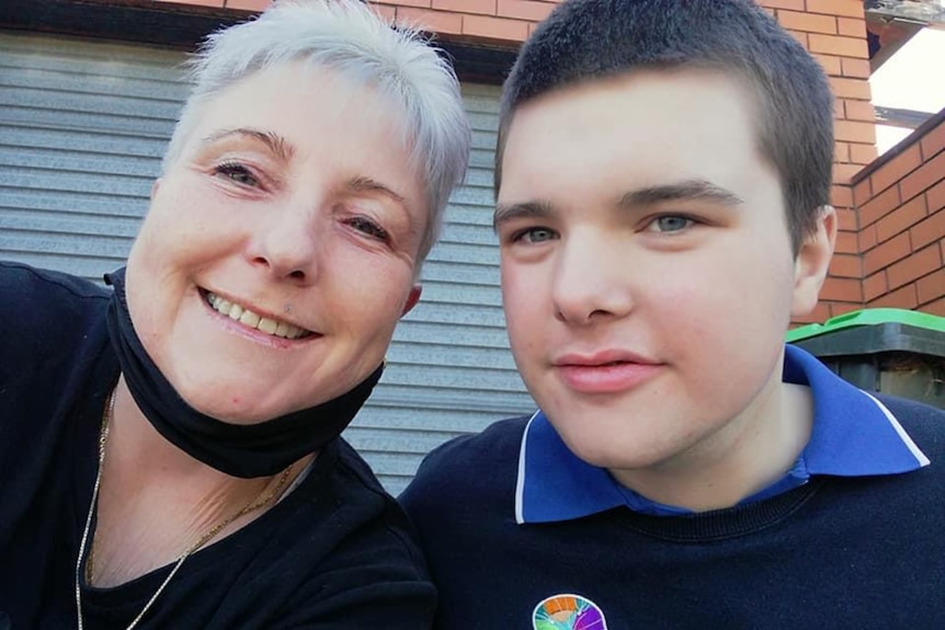 Boy in school uniform with woman smiling by side.