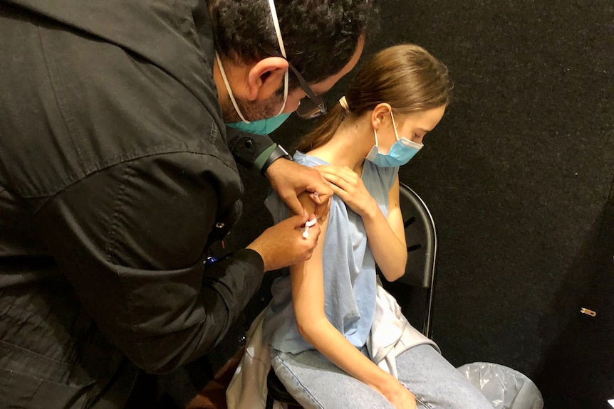 A male nurse gives a vaccine to a girl wearing a face mask.