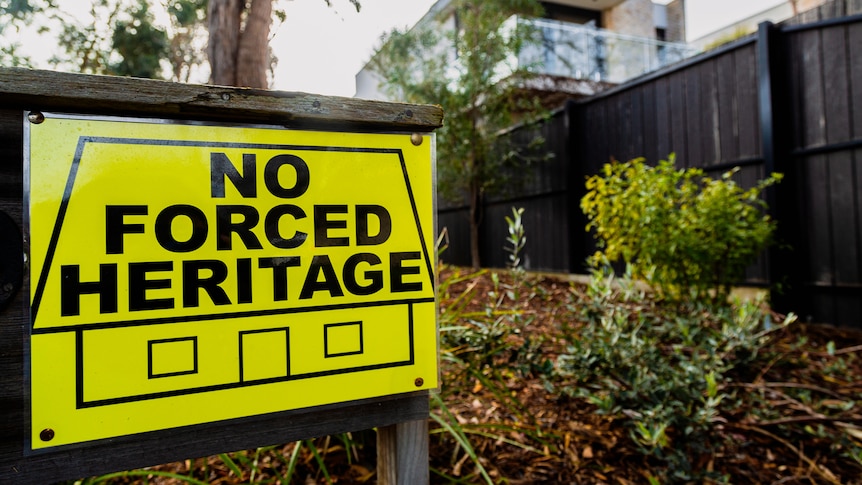 A black and yellow sign saying 'no forced heritage' in front of a house.