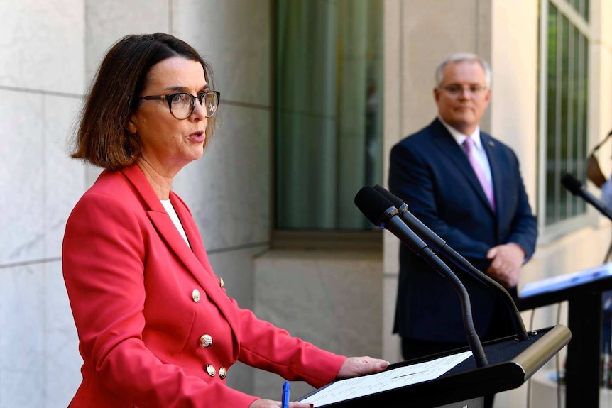 A woman and man in suits addressing media conference behind podiums with microphones.