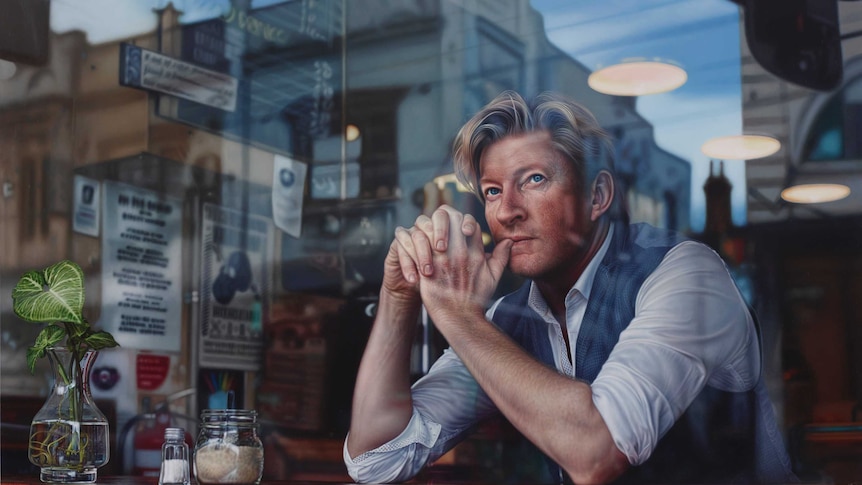 Wenham is seen through a cafe window, staring pensively into the middle distance.