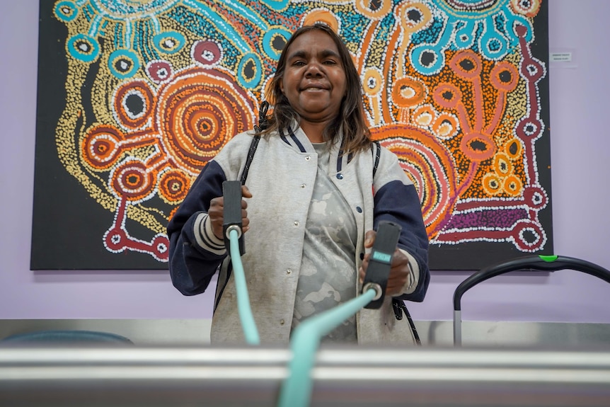A woman stands in front of Aboriginal artwork pulling exercise straps.
