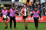 An AFL player is flanked by club medical staff as he comes off the ground after collapsing.