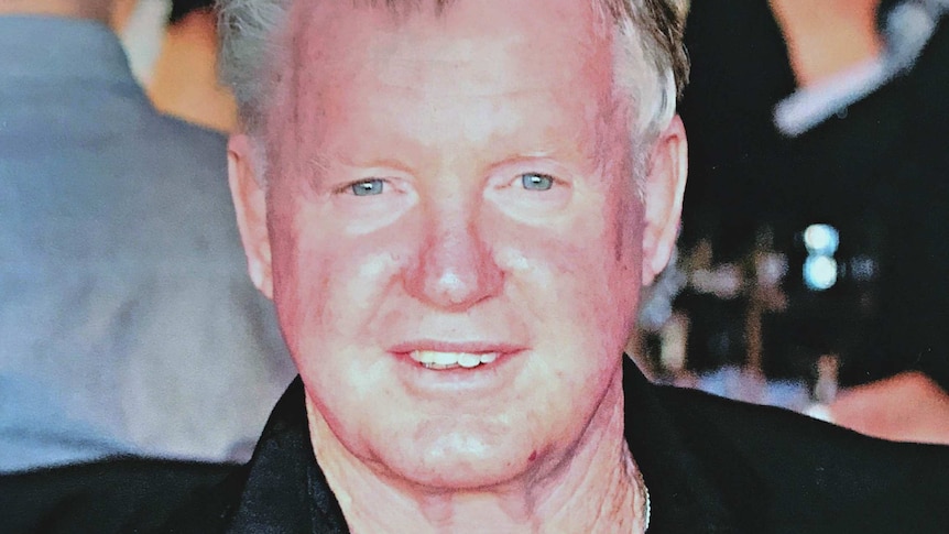 A head and shoulders shot of a middle-aged man with reddish face and white/grey hair.