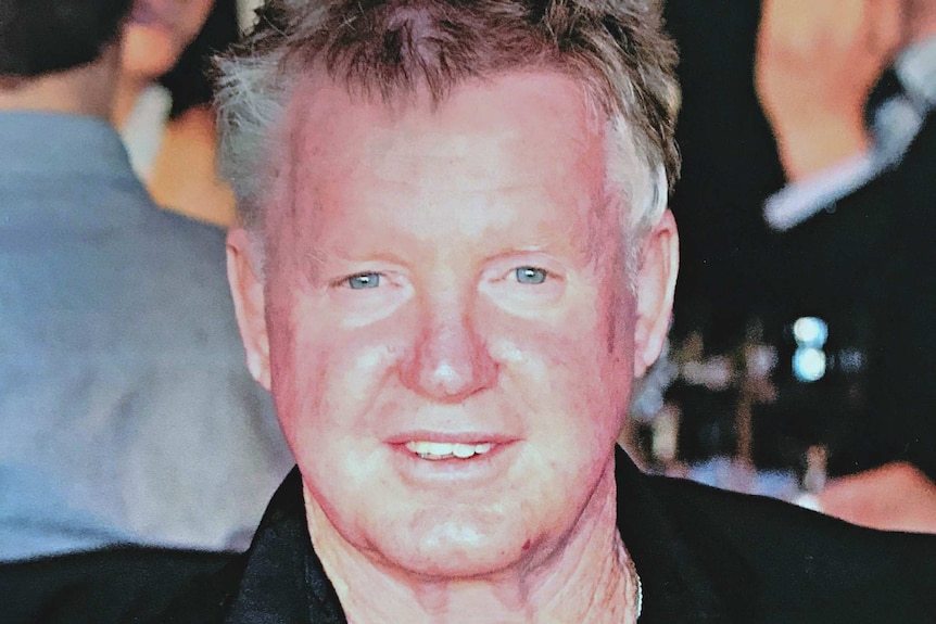 A head and shoulders shot of a middle-aged man with reddish face and white/grey hair.
