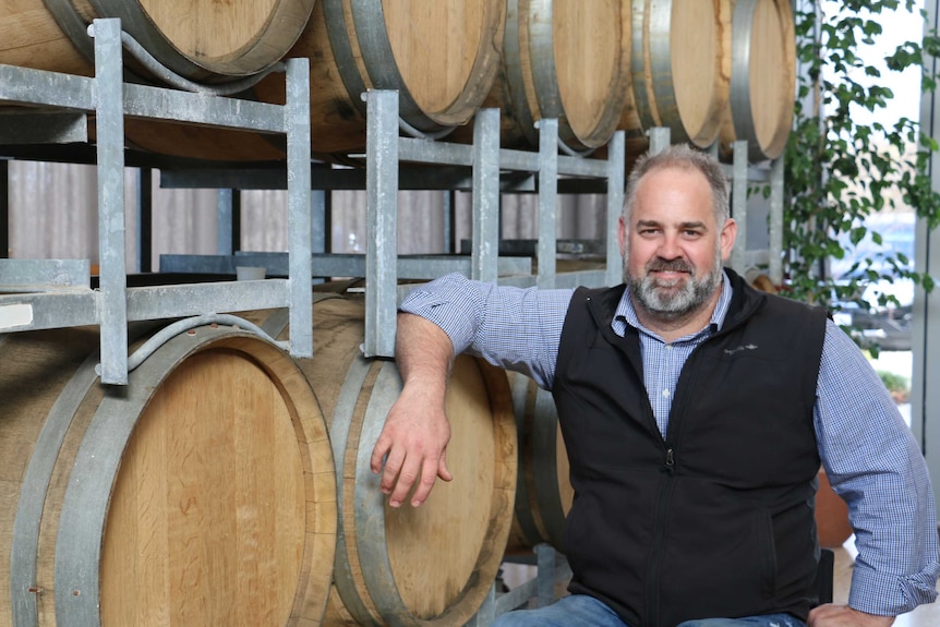 A man stands in front of a shelf full of wooden wine barrells.