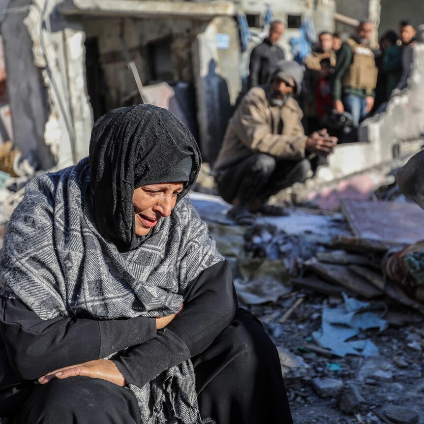 A woman sits amongst damaged homes caused by Israeli air strikes, on January 18, 2024 in Rafah, Gaza.